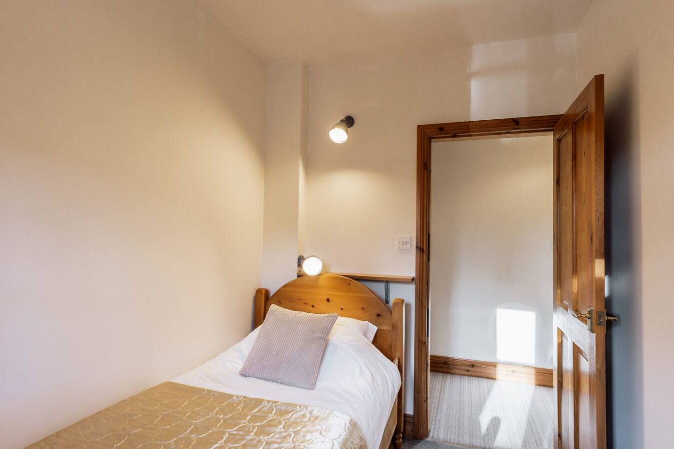 A bedroom with a wooden headboard, a bed with white bedding, a bedside table with a lamp, and a door.