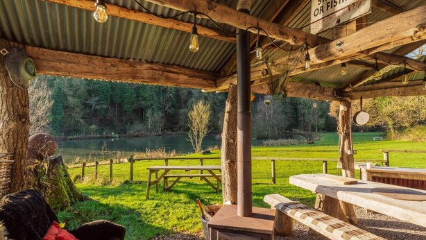 A rustic outdoor seating area with a wooden table, benches, and a sign prohibiting shooting or fishing. - Clinkum Cottage Swimming Lake, BBQ hut, Games Room (Alton Towers & Staffordshire Villages)