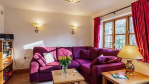 A living room with a purple sofa, a wooden coffee table, a lamp, and a bookshelf. - Bolt Hole: Swimming Lake, BBQ hut, Games Room (Alton Towers & Staffordshire Villages)