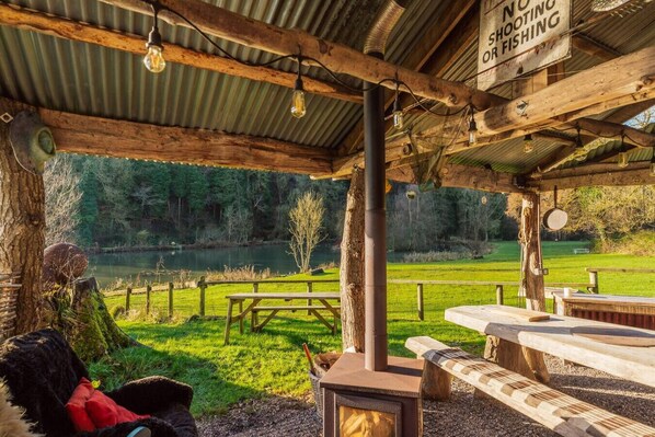 Un espace extérieur rustique aménagé avec une table et des bancs en bois, une cheminée et un panneau indiquant qu’il est interdit de chasser ou de pêcher.
