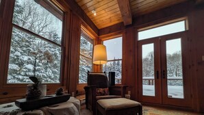 Un intérieur de chalet chaleureux, avec un revêtement en bois, de grandes fenêtres, une cheminée et un coin salon confortable.