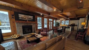 Un intérieur chaleureux de chalet en bois, avec une cheminée en pierre, un canapé en cuir et un coin repas en bois.