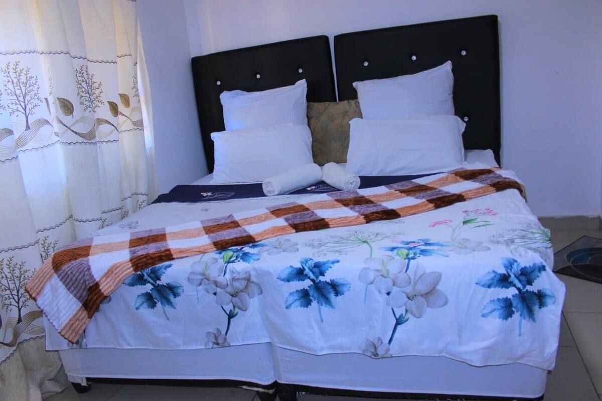 A double bed with a floral bedspread, two white pillows, and a checkered blanket.