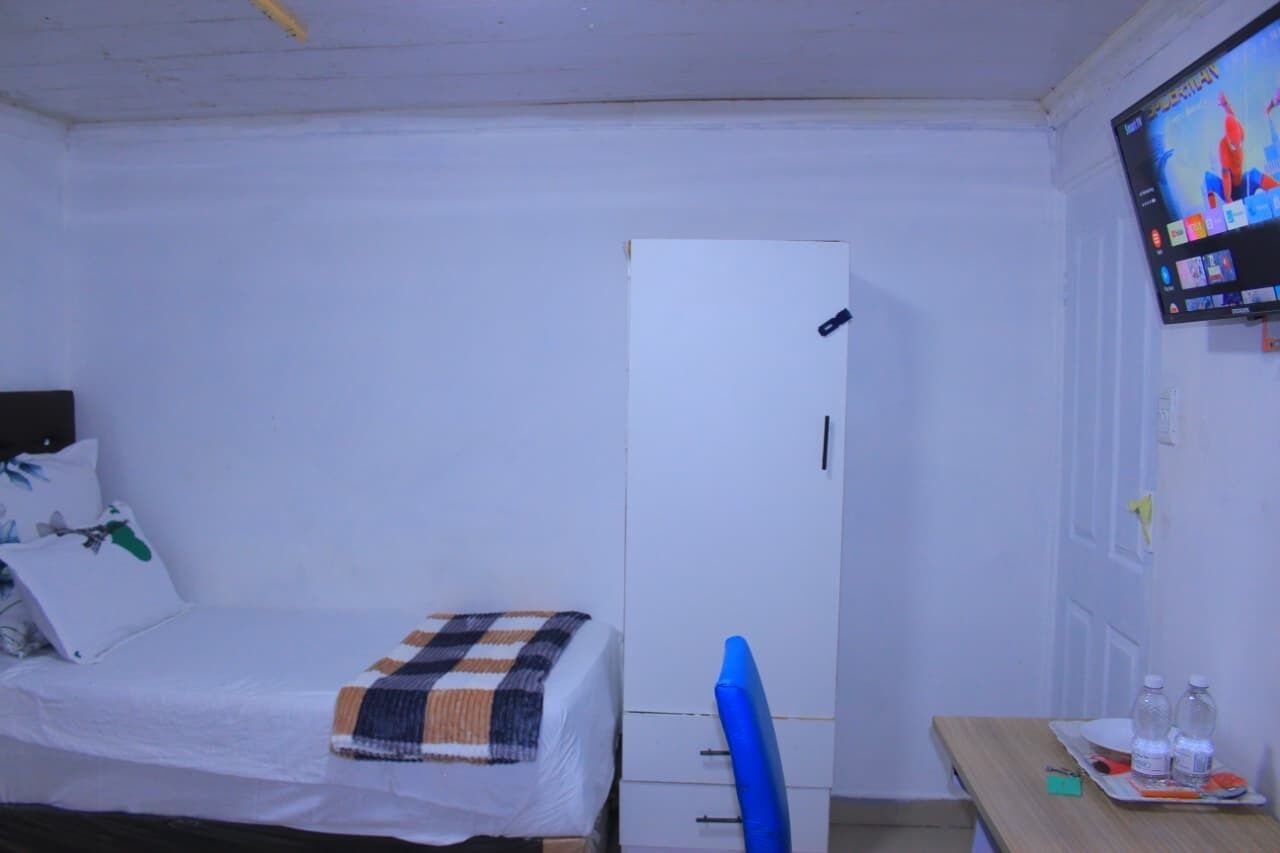 Een kamer met een bed, een kledingkast, een bureau met stoel, en een aan de muur bevestigde televisie.