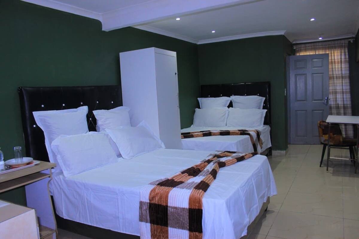 A hotel room with two beds, a wardrobe, a desk with a chair, and a dining table.