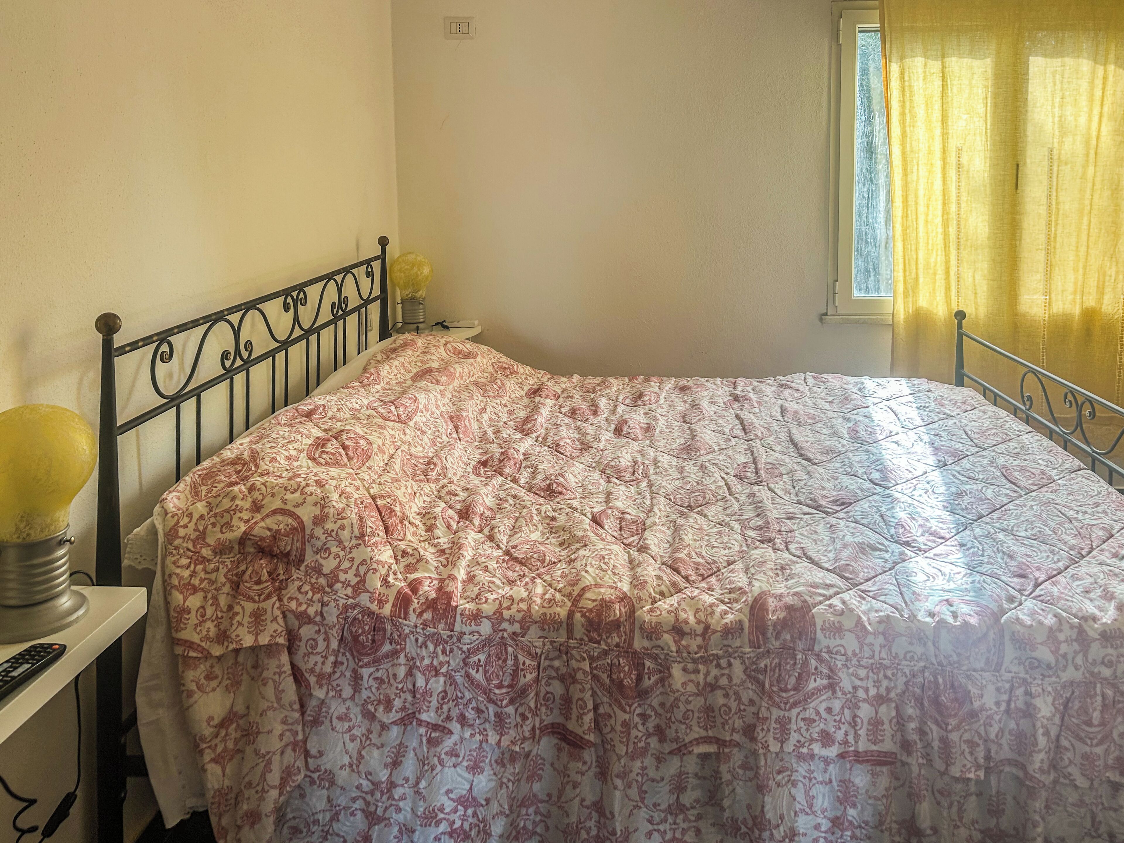 Una cama con una colcha estampada, una lámpara de noche y una ventana con cortinas.