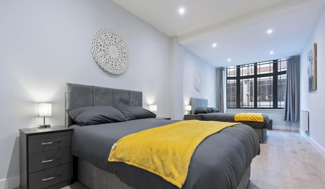 A modern bedroom with a large bed, bedside tables, a window with curtains, and decorative wall art.