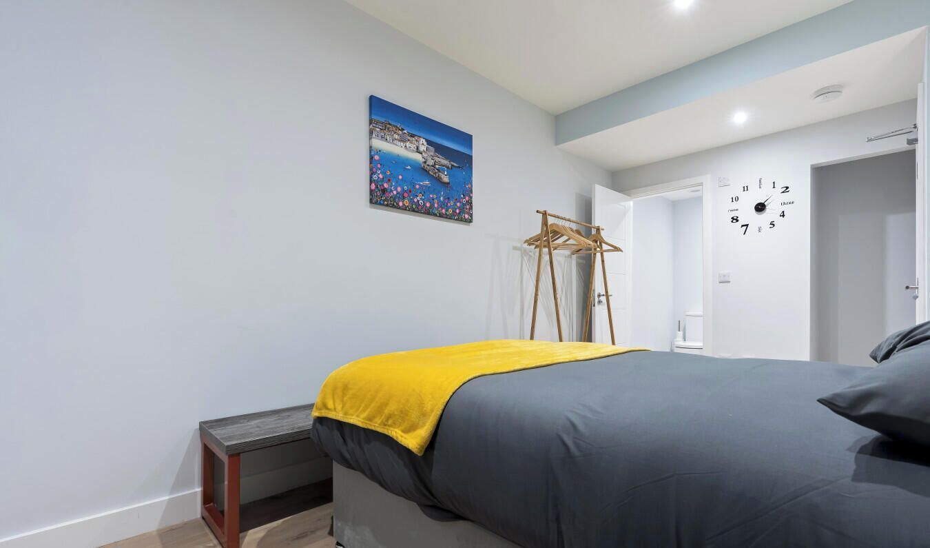Een slaapkamer met een bed, een wandklok, een deur en een schilderij.