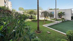 A courtyard with a lawn, palm trees, and a modern building with balconies. - Antibes Center Near the Sea: 2BR, Terrace, Parking, Wi-Fi (Antibes)