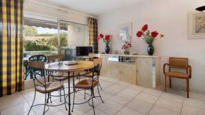 A dining area with a table and chairs, a television, and a vase with flowers. - Antibes Center Near the Sea: 2BR, Terrace, Parking, Wi-Fi (Antibes)