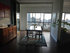 Un comedor con una mesa y sillas, vista a un paisaje urbano a través de amplios ventanales, y un mueble de madera.