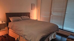 Ein Schlafzimmer mit Bett, Nachttisch, Lampe und Rollläden.