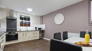 A modern kitchen with white cabinets, a black stove, and a dining area with a table and chairs. - Elaine`s Central Stay (Nottingham)