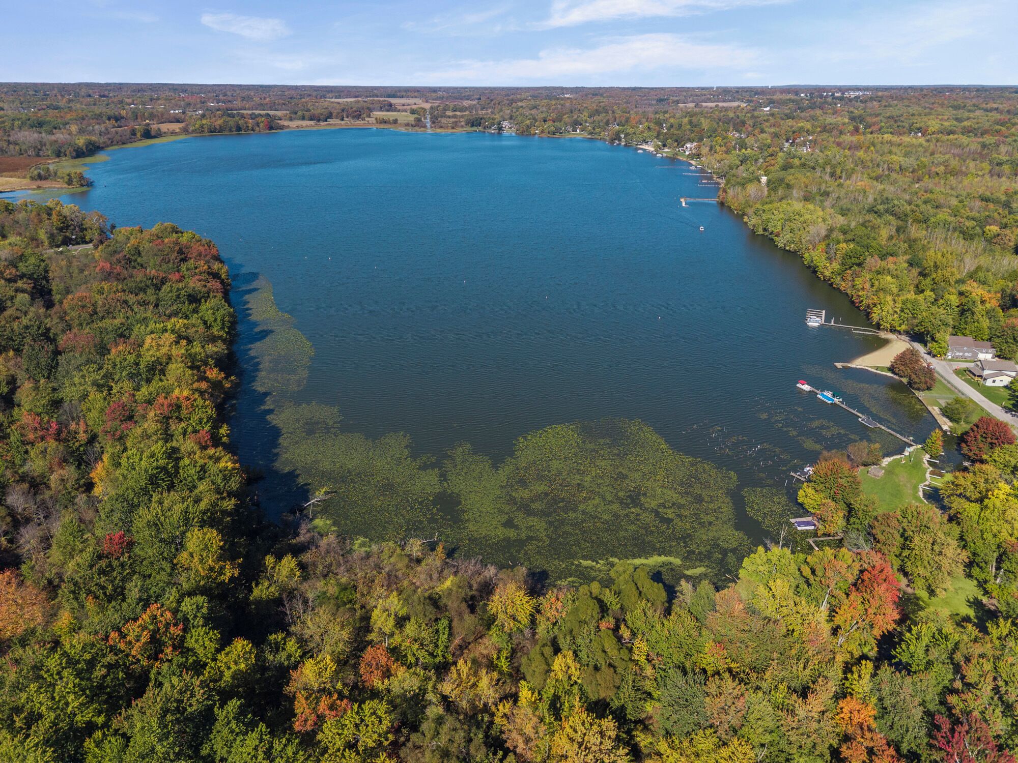 A large lake surrounded by dense forest with a dock and a small building.