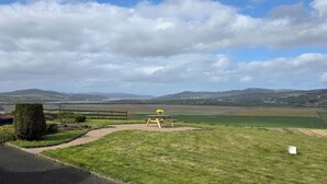 A picnic area with a bench and a table, surrounded by grassy fields and distant hills. - An Grianán Getaway (Burt)