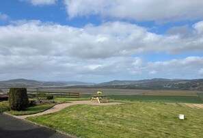 A picnic area with a bench and a table, surrounded by grassy fields and distant hills. - An Grianán Getaway (Burt)