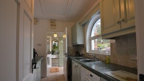 A compact kitchen with a washing machine, a sink, and a window overlooking a garden. - An Grianán Getaway (Burt)