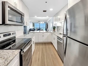 A modern kitchen with stainless steel appliances, white cabinetry, and a wooden floor. - Beach Break  3 bed 3 bath (Navarre Beach)