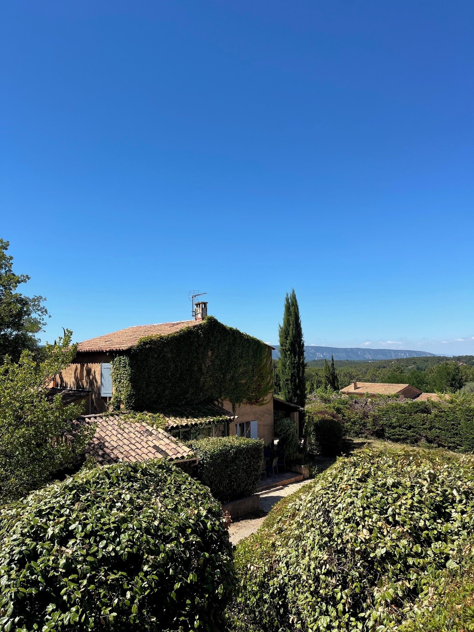 A villa with a tiled roof, surrounded by lush greenery and a clear blue sky.