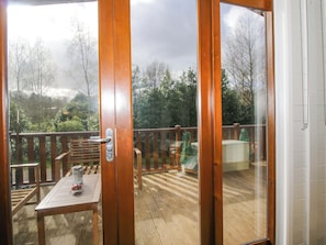 Une terrasse en bois avec une table et des chaises, une rambarde en métal et une vue sur les arbres et les collines.