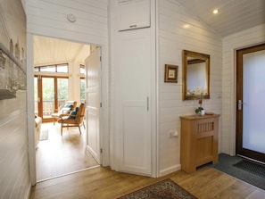 A hallway with a wooden floor, a white door, a wooden bench, and a small wooden cabinet with a mirror. - No.14 Astbury Falls Luxury Retreat (Bridgnorth)