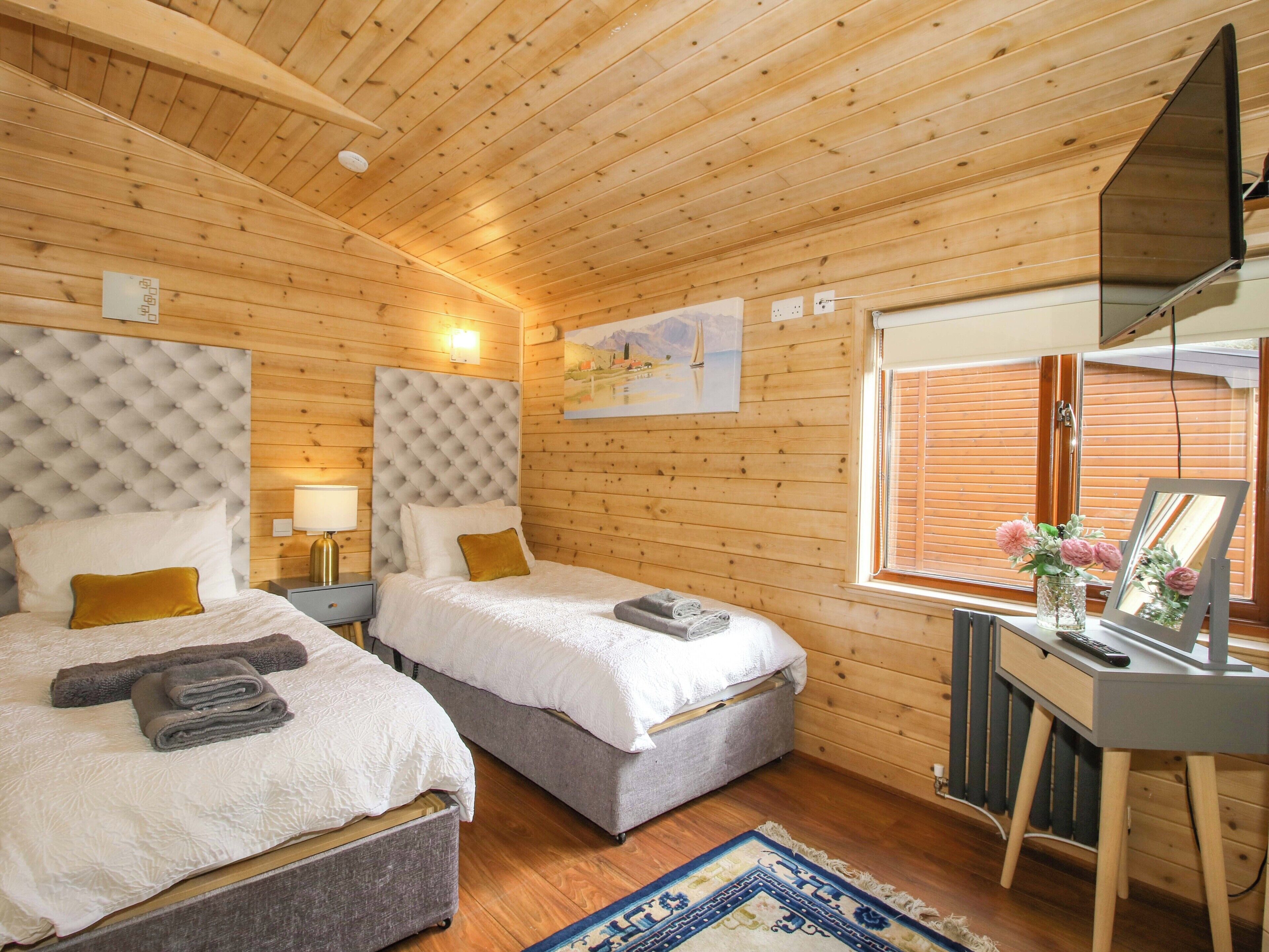 Un dormitorio de cabaña de madera con dos camas, un escritorio y una ventana.
