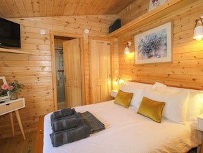 Une chambre dans un chalet en bois, comprenant un lit, des serviettes, un tableau et un téléviseur.
