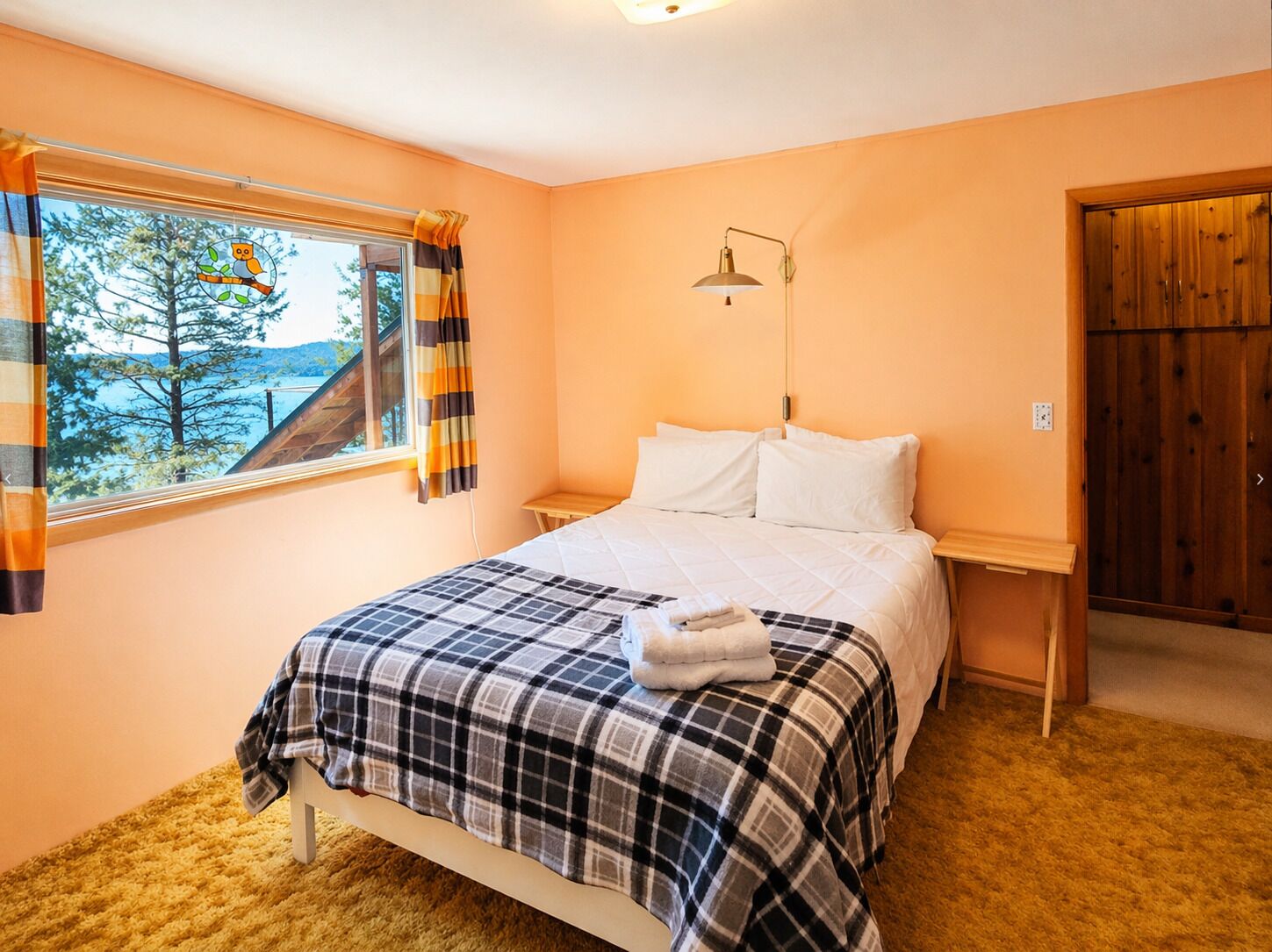 A bedroom with a bed, a window with curtains, a bedside table, and a door.