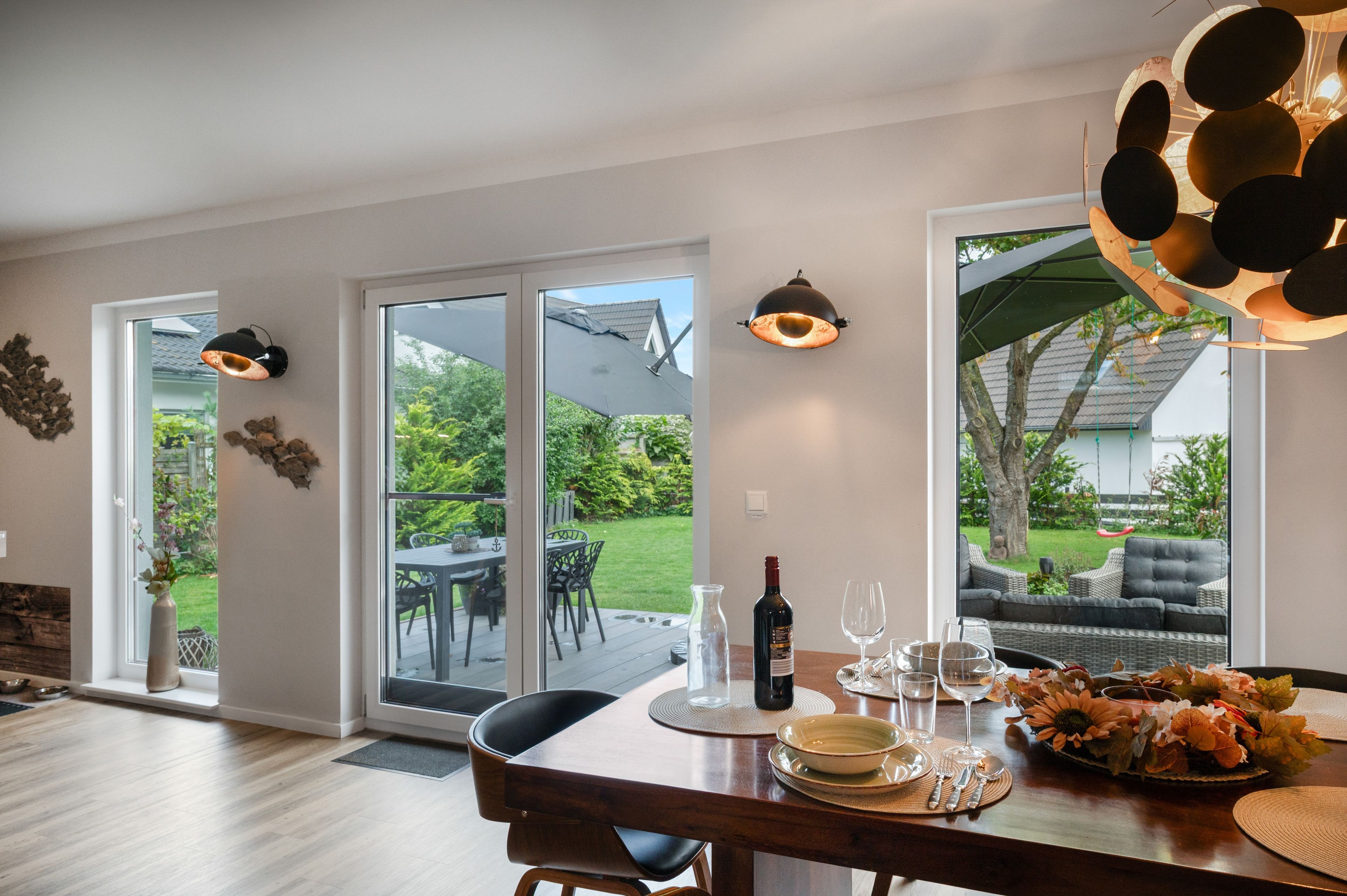 A dining area with a table set for two, a bottle of wine, and a vase of flowers.