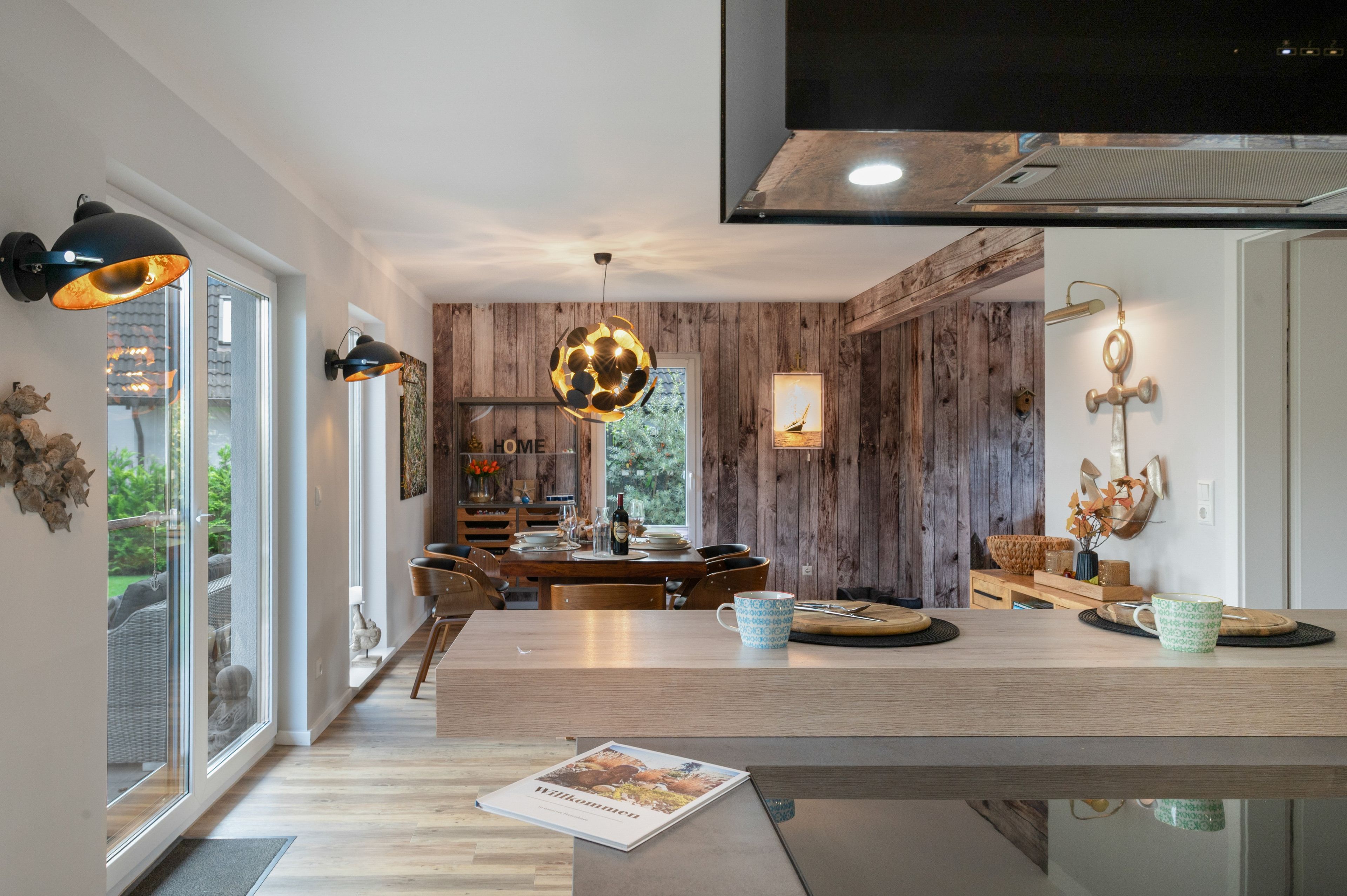 A modern kitchen with a wooden accent wall, a dining table set with chairs, and a large window providing a view of the outdoors.