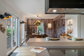 Une cuisine moderne avec un mur d’accent en bois, une table à manger avec des chaises, et une grande fenêtre offrant une vue sur l’extérieur.