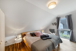 A bedroom with a bed, bedside table, lamp, chair, and a view of the outside.