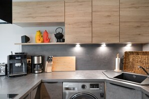 Eine moderne Küche mit Holzschränken, einer Kaffeemaschine, einem Wasserkocher und einer Waschmaschine.