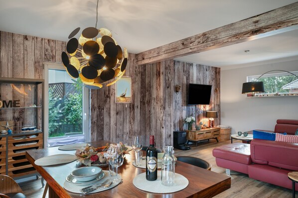 Un salon moderne avec un mur en bois, un coin repas avec une table en bois dressée pour deux personnes, et un canapé rouge.
