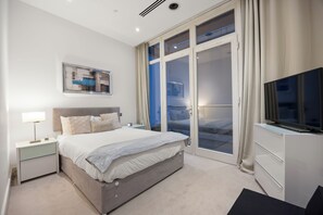 Ein modernes Schlafzimmer mit Bett, Nachttisch, Fernseher und einem großen Fenster mit Vorhängen.
