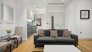 A modern living room with a grey sofa, a white coffee table, and a dining area with a glass table and chairs. - The Monument Retreat near Bank Station (London)