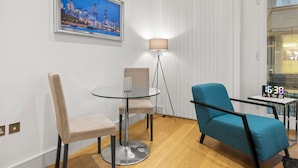 A modern room with a glass table, two chairs, a lamp, and a clock. - The Monument Retreat near Bank Station (London)