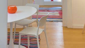A room with a white table, two chairs, a colorful rug, a white bookshelf, and a door leading to another room. - Adenzia Apartment (Palermo)