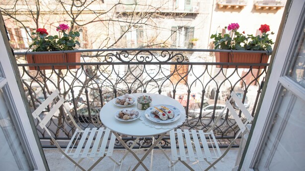 A balcony with a table set for two, surrounded by a wrought iron railing, and potted plants on the railing. - Adenzia Apartment (Palermo)