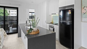 A modern kitchen with a black refrigerator, white cabinets, and a central island with a plant.
