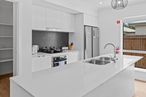 Una cuina moderna amb armaris blancs, un frigorífic d'acer inoxidable, un forn de sobre i una illa gran amb una brossa.