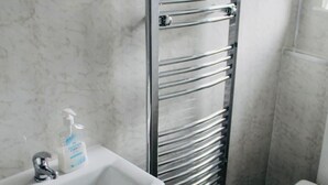 A bathroom with a white sink, a chrome towel rack, a toilet, and patterned floor tiles. - Room-charming BnB Retreat in East Riding (Withernsea)