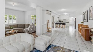 Un grand espace de vie comprenant un canapé, un fauteuil, une table basse et une cuisine en arrière-plan.