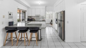 Une cuisine moderne avec des meubles blancs, un réfrigérateur en acier inoxydable et un îlot central doté de tabourets de bar.