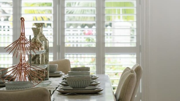 Un coin repas avec une table dressée pour quatre personnes, un lustre et une vue dégagée sur l’extérieur grâce à de grandes fenêtres.