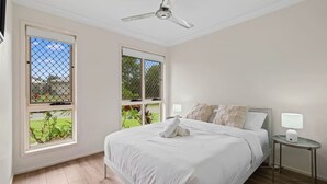 Ein Schlafzimmer mit einem Bett, zwei Nachttischen, einem Deckenventilator und großen Fenstern.