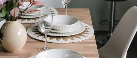 Mesa de jantar posta com pratos brancos, copos e um vaso com flores.