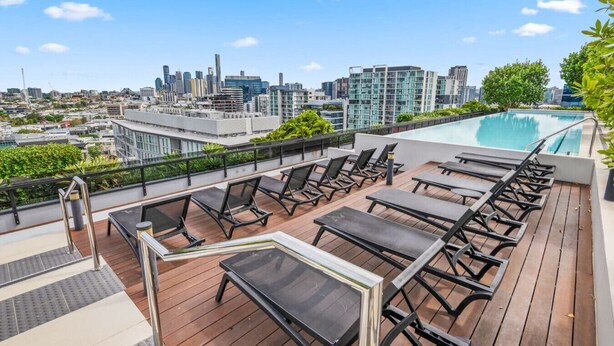 Terraza en la azotea con piscina, sillas de descanso y vistas al horizonte de la ciudad.