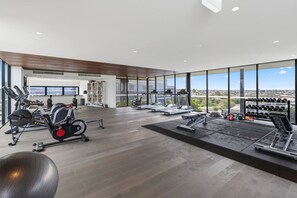A modern gym with cardio machines, weightlifting equipment, and a view of the city. - Premium Urban Stay – Rooftop Pool, City Vista (Newstead)