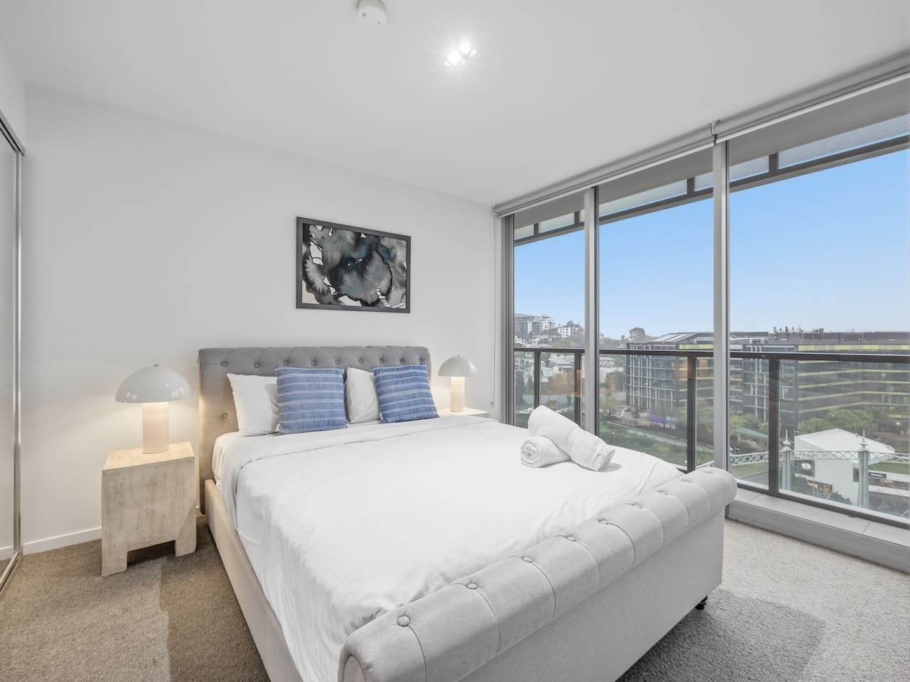 Een moderne slaapkamer met een groot bed, uitzicht op de stad en een schilderij aan de muur.